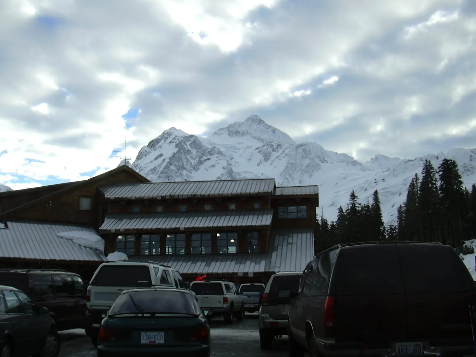 Day lodge at the White Salmon base area of Mt. Baker Ski Area in winter, seen across a full parking lot with Mount Shuksan behind